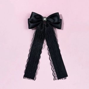 Detail of black satin bow with oval crystal gemstone and delicate lace streamers