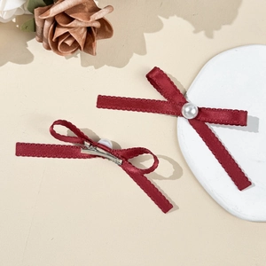 Détail de deux pinces à cheveux en satin bordeaux avec perles sur fond minimaliste