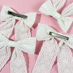 Detailed view of four white lace bow hair clips featuring delicate floral patterns on pink
