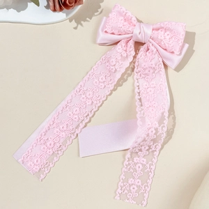 Detail of pink lace bow hair clip showing delicate fabric texture and long flowing ribbons