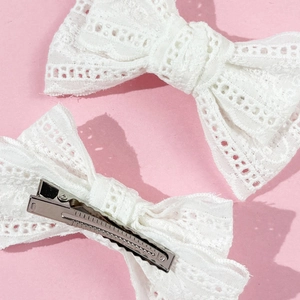 Close-up of white lace bow hair clips with metal alligator grip and floral embroidery