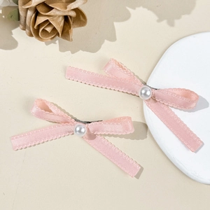 Vue détaillée de barrettes nœuds en satin rose avec perles blanches sur fond texturé