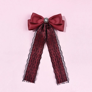 Detailed macro view of the burgundy satin bow with an elegant gemstone and black lace ribbon