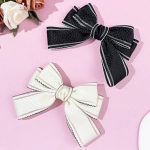 Elegant bow hair clips with lace trim in black and cream on a pink background