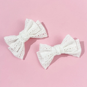 Detailed close-up of two white lace bow hair clips showing delicate hollow texture on pink