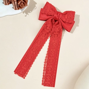 Detailed view of red satin and lace bow hair clip with elegant long wavy ribbon streamers