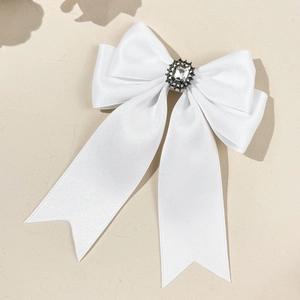 Detail of a white satin bow hair clip with a sparkling rectangular rhinestone center