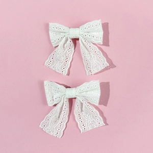 Set of two white lace bow hair clips with hollow floral pattern on pink background