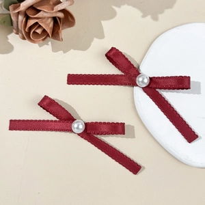 Paire de barrettes nœuds en satin rouge avec perle sur un fond rustique élégant
