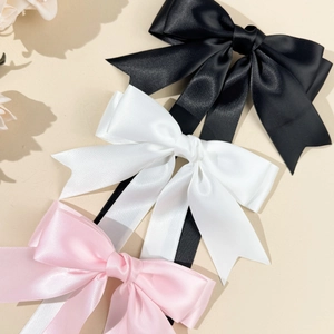 Dettaglio dei fermagli per capelli con fiocco in raso nero, bianco e rosa setoso