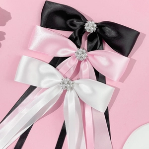 Detail view of satin bow hair clips with pearls and long ribbons in pink, black, and white