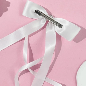 Detail of white satin bow hair clip with long ribbons and a silver metal duckbill clamp