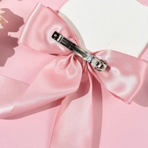 Détail du nœud en satin rose montrant la texture de soie et la pince en métal