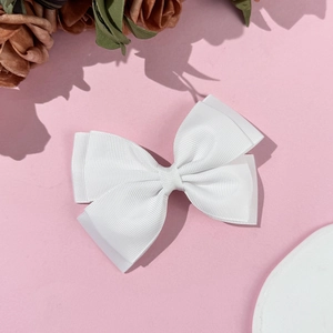 Close-up detail of a white grosgrain ribbon bow hair clip on a soft pink background