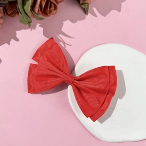 Detail of red grosgrain ribbon bow hair clip displayed on a white decorative plate
