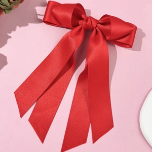 Elegant red satin bow hair clip with flowing ribbons and silk finish on a pink base