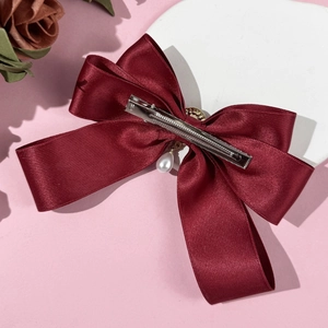 Detail of burgundy satin bow hair clip with white faux pearl pendant and metal duckbill clip
