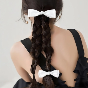 Detail of two white satin double-layered bow hair clips worn on a braided ponytail