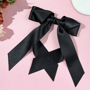 Elegant large black satin bow hair clip with long ribbons on a pink background