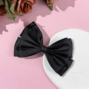 Detailed view of black grosgrain ribbon bow hair clip on a white stone coaster