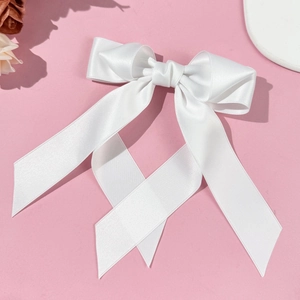 Macro detail of the smooth white satin ribbon bow hair clip with elegant long streamers