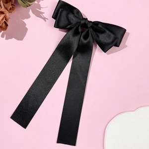 Detailed view of elegant black satin bow hair clip with long ribbons on pink background