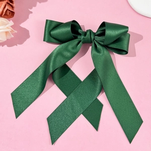 Close-up of a dark green satin bow hair clip with long ribbons on a pink background