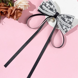 Detail of elegant black and white lace bow hair clip with pearl pendant and long ribbons