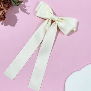 Detail view of cream satin bow hair clip with long ribbons on soft pink background