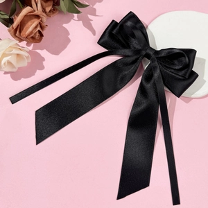 Elegant black satin bow hairclip with long ribbons on soft floral background