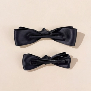 Detail of two black satin bow hair clips showing textured fabric and metal alligator clips