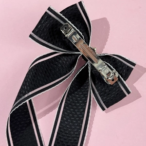 Détail du nœud noir avec bords roses et barrette à ressort en métal argenté au dos