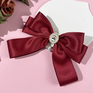 Close-up of burgundy satin bow hair clip with crystal center and teardrop pearl detail