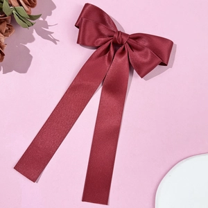 Close-up of wine red satin bow hair clip with long silk ribbons on a soft pink background