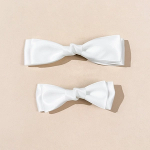 Detail view of two cream satin bow hair clips in different sizes on beige surface