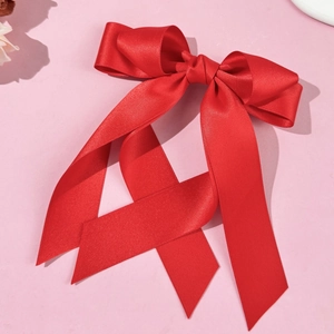 Close-up of a vibrant red silk satin ribbon bow with long tails on a pink surface