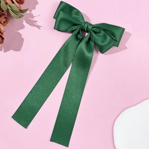 Close-up of dark green satin bow hair clip with long ribbons and silky texture finish