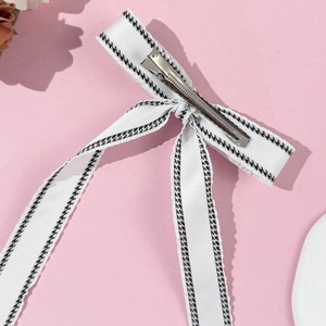 Detail of white ribbon bow hair clip with black houndstooth trim and silver duckbill clip