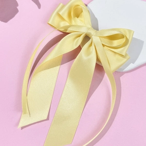 Elegant yellow satin bow hair clip with long ribbons on white stone platform