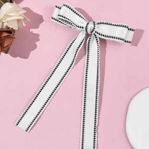 Detail of elegant white bow hair clip with black houndstooth pattern on a pink background