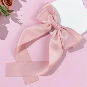 Detail of pink satin bow hair clip with long ribbons on a minimalist background