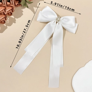 Detailed view of white satin bow hair clip with pearl rhinestone center and long ribbons