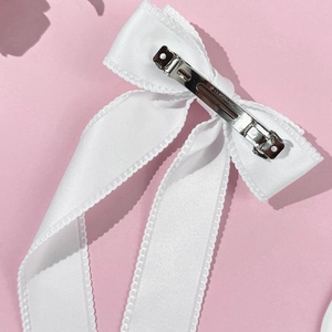Detail view of white satin bow hair clip with silver metal spring mechanism and engraving