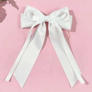 Detailed view of white satin bow hair clip with long ribbons on pink background