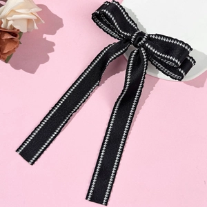 Detailed view of black bow hair clip with white edge stitching and long flowing ribbons