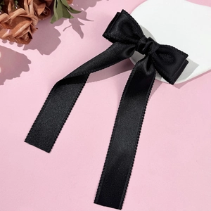 Elegant black satin bow hair clip with long ribbons on a minimalist display stand
