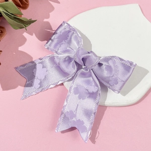 Detail der violetten Satin-Haarschleife mit Kleemuster und gezackten Nähten am Rand