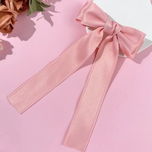 Detail of pink silk satin hair bow with scalloped edges and long flowing ribbons