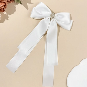 Close-up of white satin bow hair clip with elegant pearl and rhinestone centerpiece