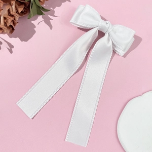 Macro shot of elegant white satin bow hair clip with wavy lace edges and long flowing ribbons